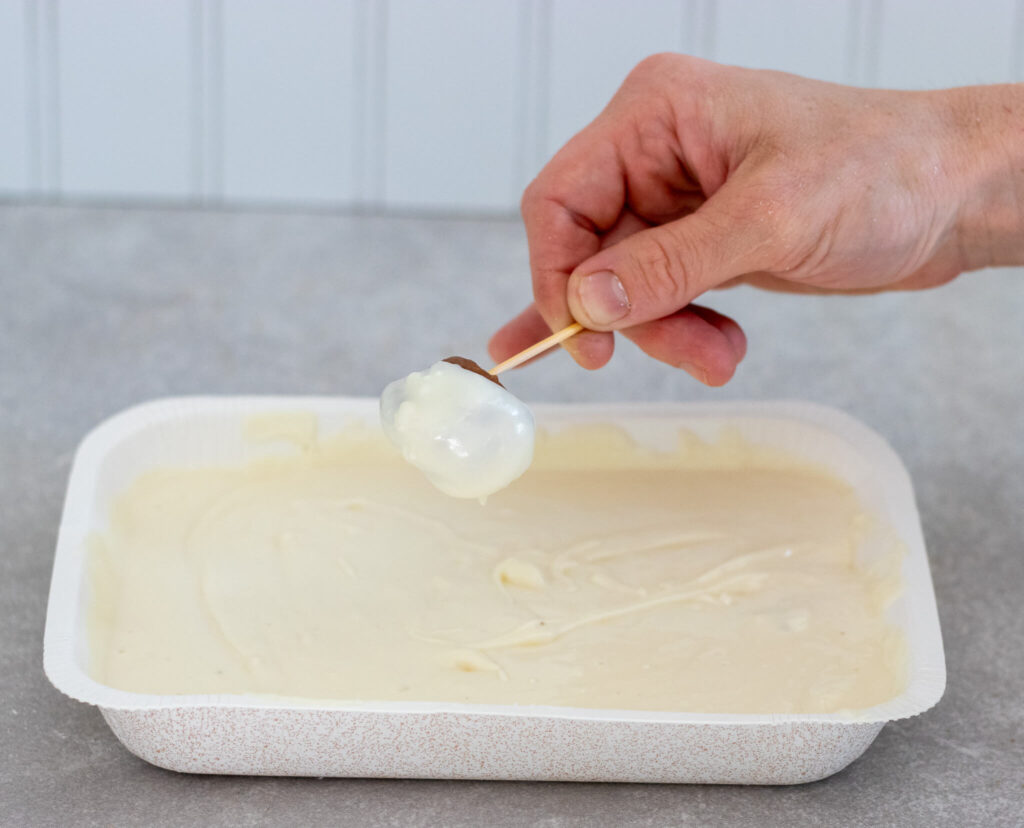 woman's hand dipping cookie butter truffle into white chocolate