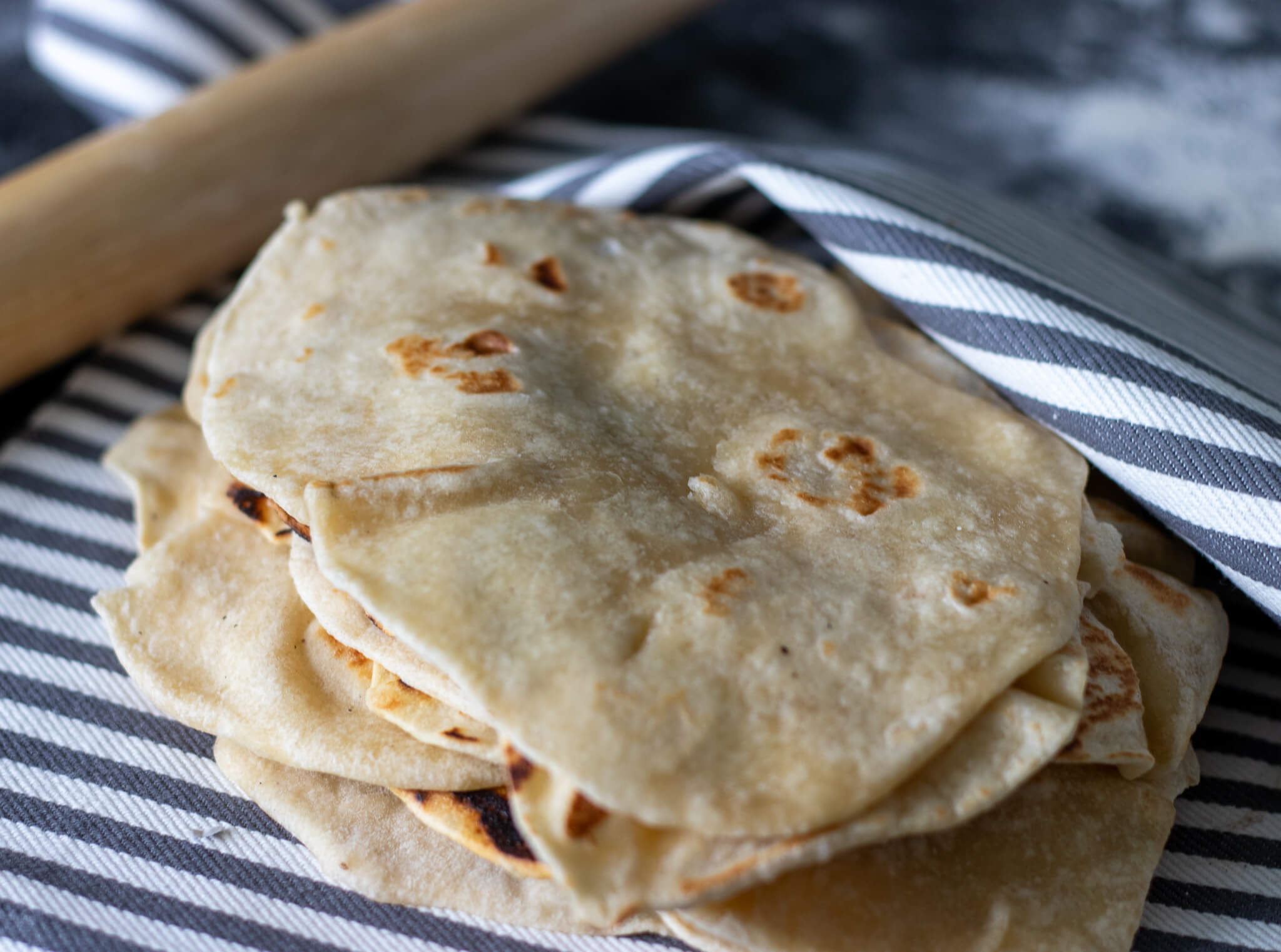 lard tortillas on a striped tea towel with a rolling pin in the background