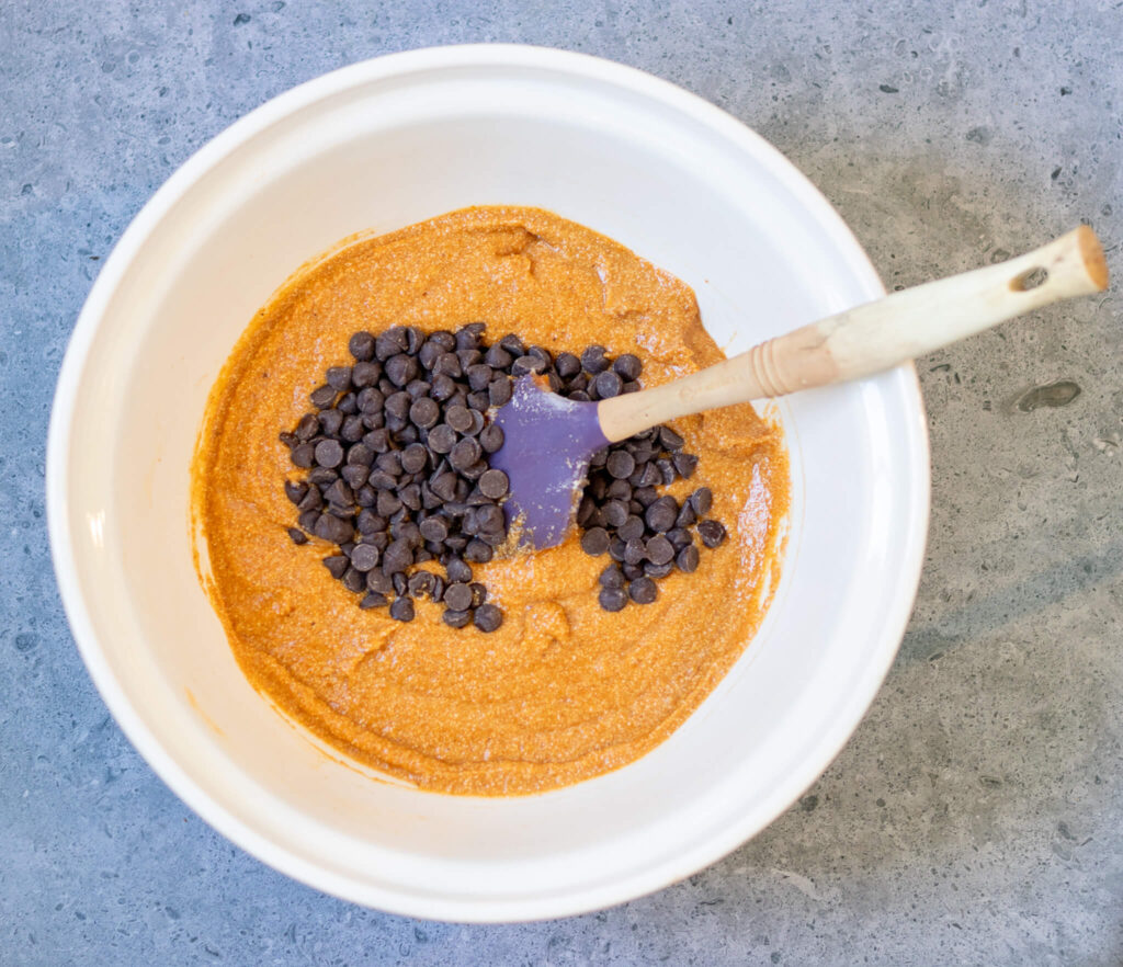 a bowl of pumpkin batter with chocolate chips being mixed in