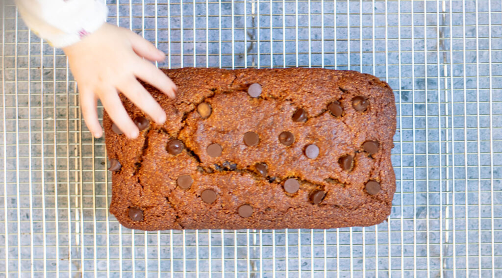 pumpkin bread on a wire rack with a baby's hand reaching for it