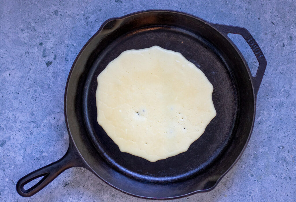 cast iron pan with a crepe poured in it looking bubbly