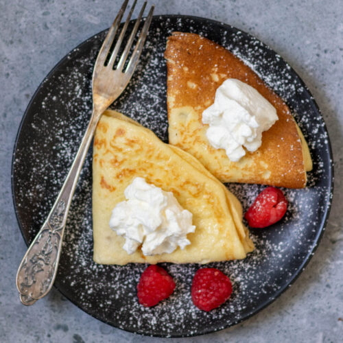 two dairy-free sourdough crepes on a plate with a fork and three raspberries