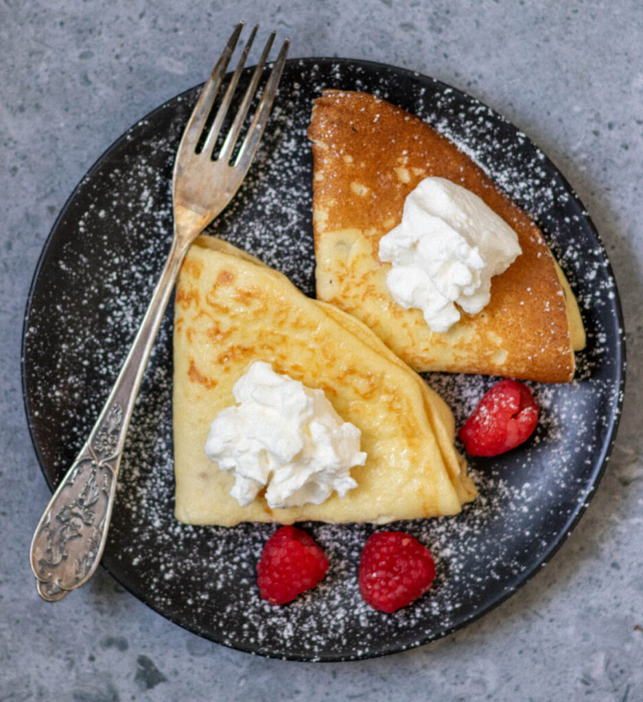 two dairy-free sourdough crepes on a plate with a fork and three raspberries