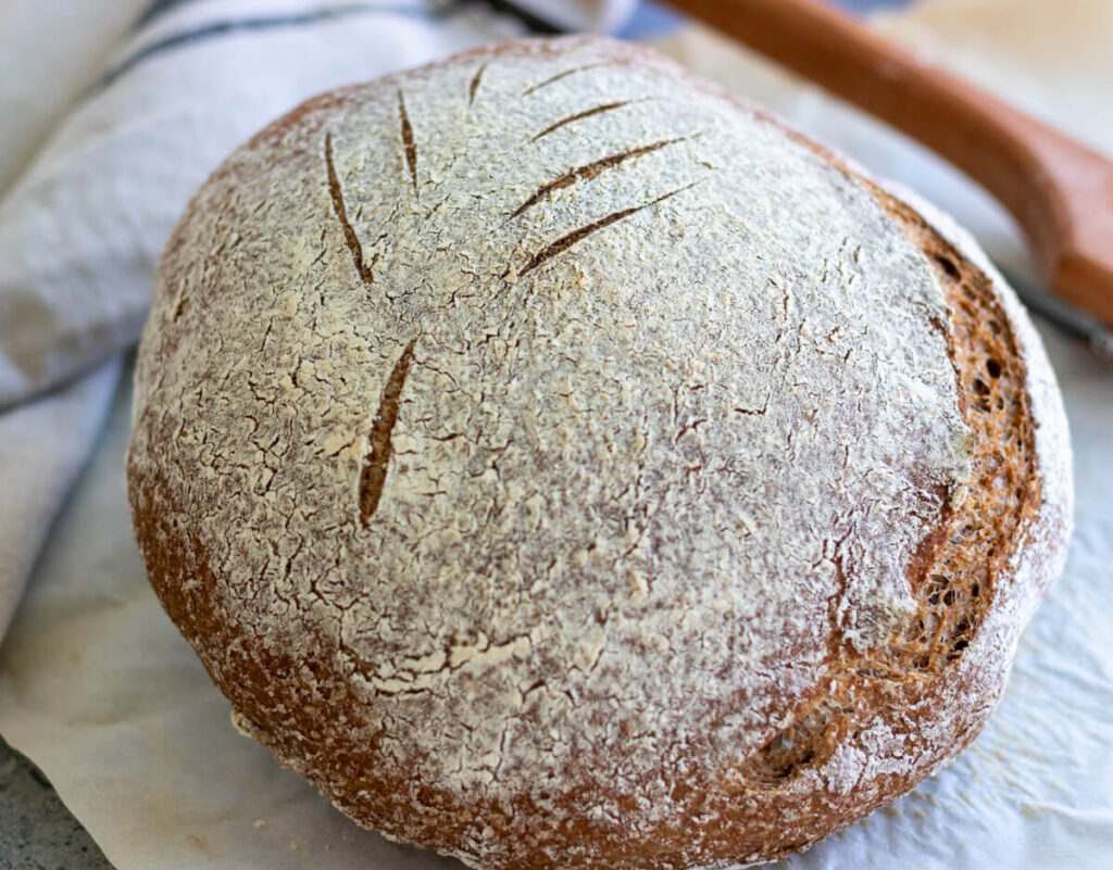 whole wheat sourdough boule sitting on a counter with knife