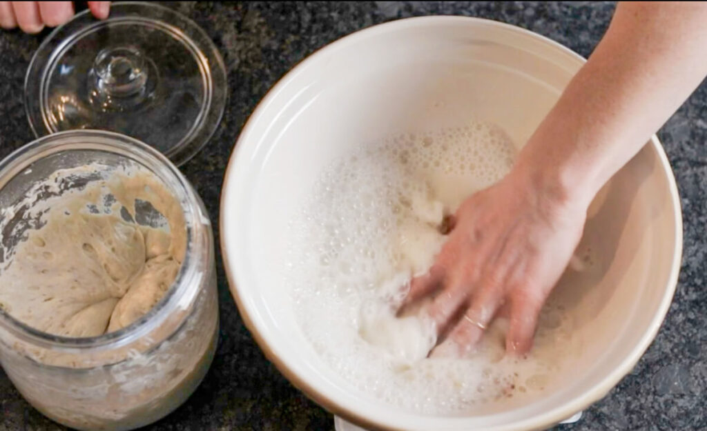 a woman's hand combining sourdough starter and water